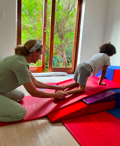 Elijah in therapy, on his hands and knees crawling up a padded ramp with a therapist assisting his legs.